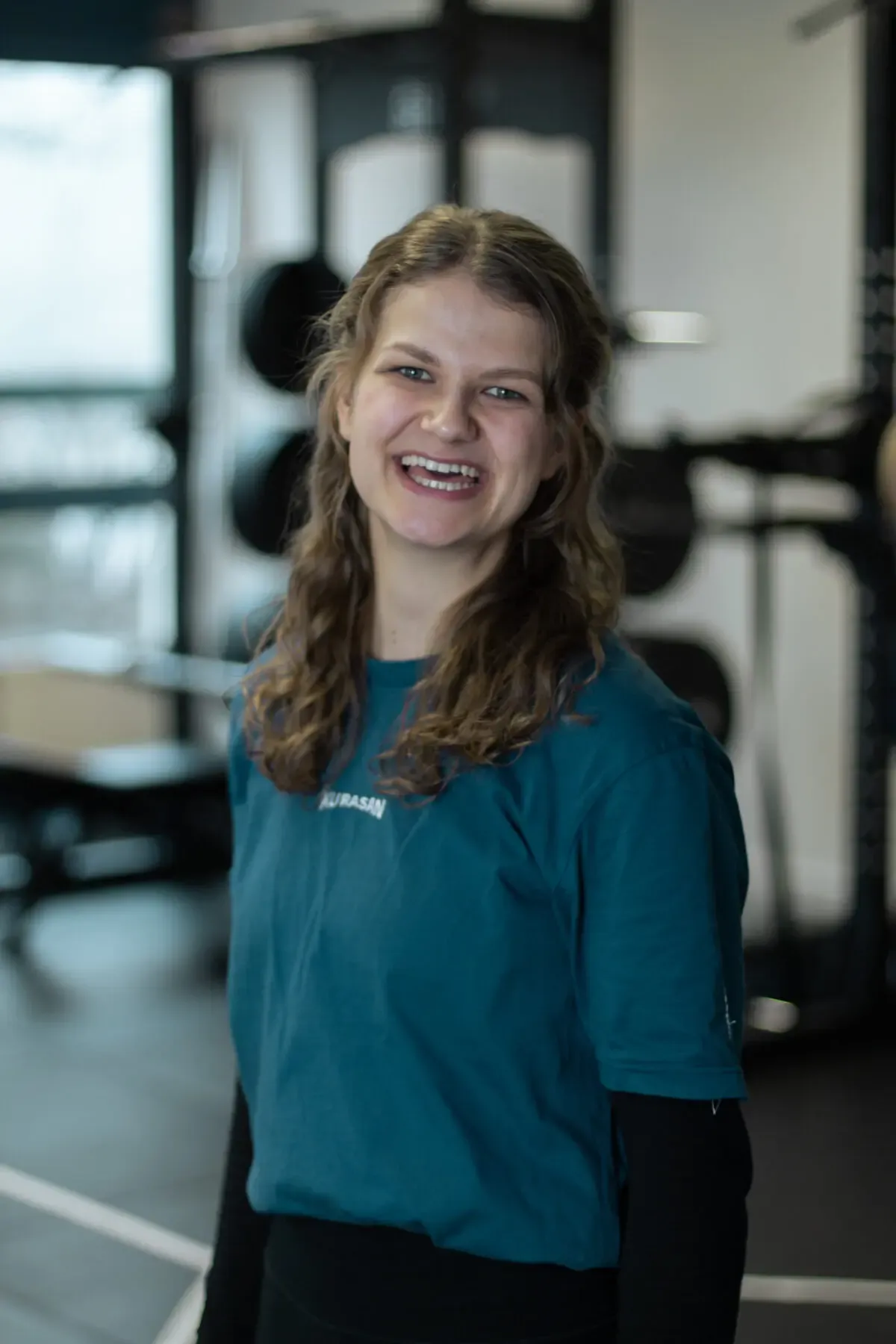 Porträt einer lächelnden Trainerin im Fitnessstudio vor Trainingsgeräten.